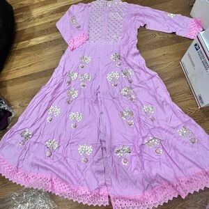 Long pink dress with golden detailing and pom poms. Slit in the middle